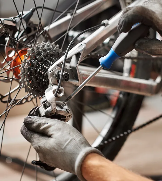 Mécanicien avec des gants ajustant le dérailleur arrière d'un vélo avec un tournevis à Nogent-sur-Marne dans le Val-de-Marne près de Montreuil 
